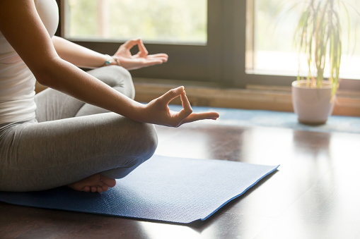 Attractive young woman working out at home, doing yoga exercise on blue mat, sitting in Easy (Decent, Pleasant Posture), meditating, breathing, relaxing. Body close-up, focus on hand
