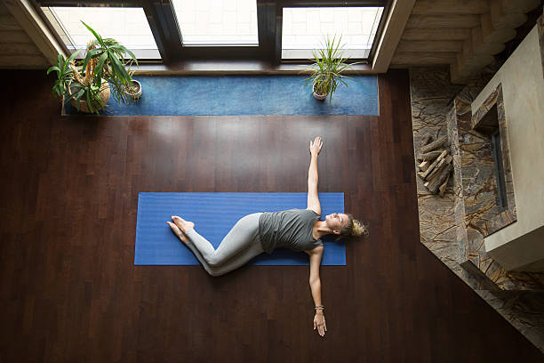 Yoga at home: Belly Twist Pose Attractive young woman working out in living room, doing yoga exercise on wooden floor, lying in Belly Twist Pose, Jathara Parivartanasana, resting after practice, full length, top view twist pose stock pictures, royalty-free photos & images