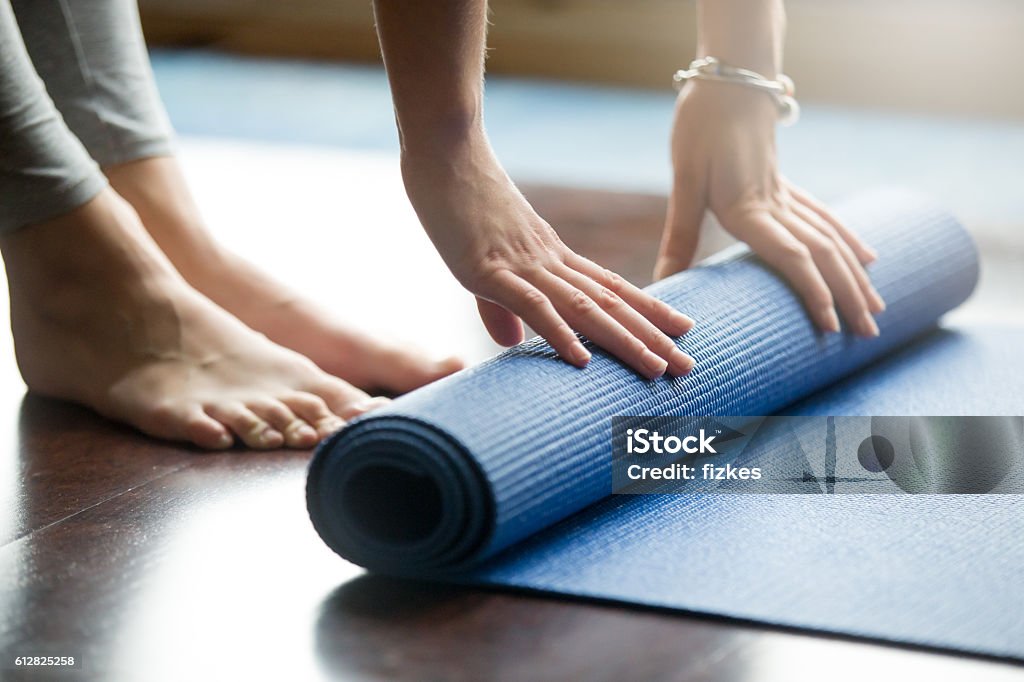 Yoga training concept Close-up of attractive young woman folding blue yoga or fitness mat after working out at home in living room. Healthy life, keep fit concepts. Horizontal shot Yoga Stock Photo