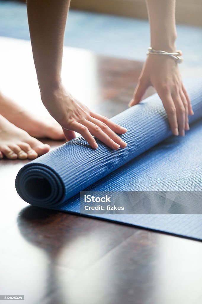 Yoga practice is over Close-up of attractive young woman folding blue yoga or fitness mat after working out at home in living room. Healthy life, keep fit concepts. Vertical image Exercise Mat Stock Photo