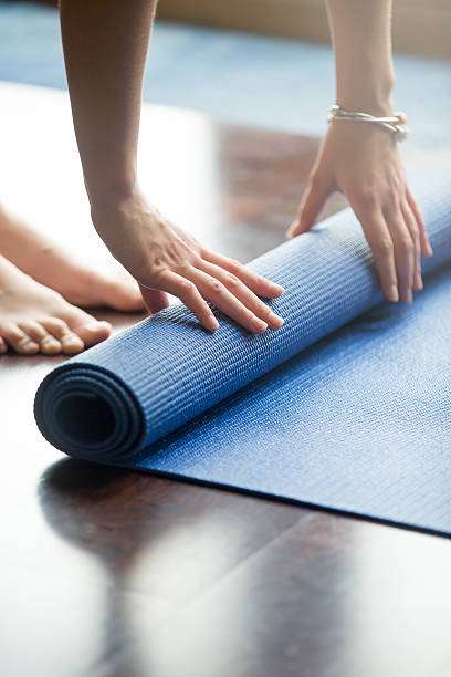 Yoga practice is over Close-up of attractive young woman folding blue yoga or fitness mat after working out at home in living room. Healthy life, keep fit concepts. Vertical image exercise mat stock pictures, royalty-free photos & images