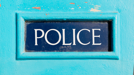 Traditional British Police sign written on dark blue background on a light blue wooden police box