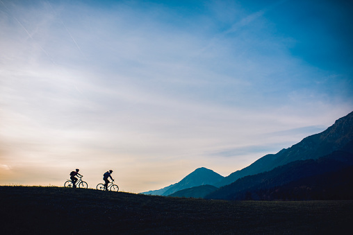 Young couple is cycling on footpath in nature. Sun is shining and mountains are in the back.