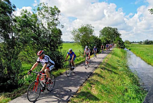 Leiderdorp, Netherlands - August 3, 2013: Group of cyclists riding on narrow roads through the polders of the green heart of the Netherlands