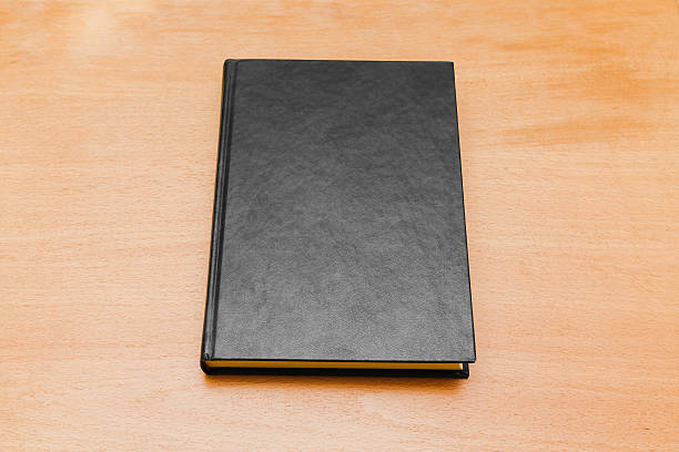 istock Book with black cover laying on wooden table 612829944