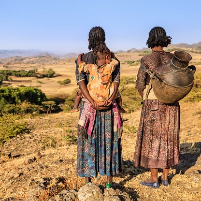 Young African women looking at view near Lalibela, Ethiopia, Africa One of them is carrying her baby, a the second woman is carrying jar of water. African women and children often walk long distances to bring back jugs of water that they carry on their back