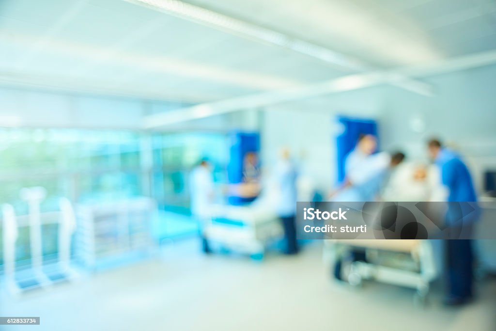 defocussed hospital ward background A  senior female nursing sister demonstrates the the various equipment on the training ward whilst a male staff nurse shows the medical mannequin to another group of medical student nurses . They are all standing around the hospital beds . The whole scene is defocussed to be used as a background Hospital Ward Stock Photo