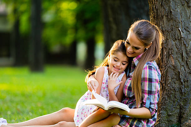 istock Mother and daughter sitting on grass reading a book. 612835728