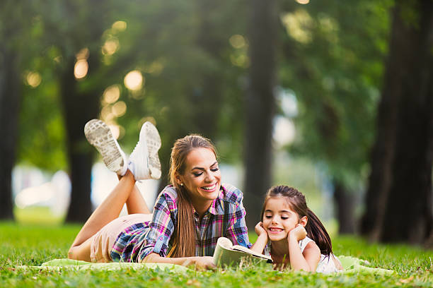 istock Mother and daughter reading book in a park 612836174
