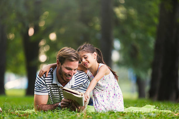 istock Father and daughter reading a book in the park 612836434