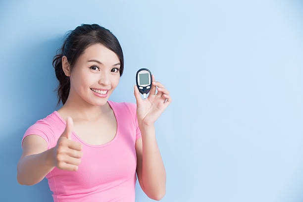 woman holding  blood glucose meter Woman holding a blood glucose meter to prevention diabetes isolated on blue background, asian sugar control stock pictures, royalty-free photos & images