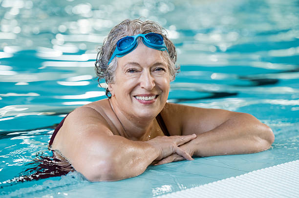 Elderly woman in pool Mature woman wearing swim goggles at swimming pool. Fit active senior woman enjoying retirement standing in swimming pool and looking at camera. Happy senior healthy old woman enjoying active lifestyle. swimming stock pictures, royalty-free photos & images