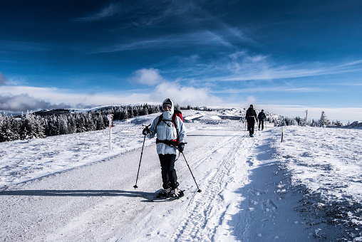 Retenegg, Austria - January 24, 2016: hikers on snowshoes on winter hiking trail near Geireck hill in Fischbacher Alpen mountain range in Styria with blue sky and clouds 
