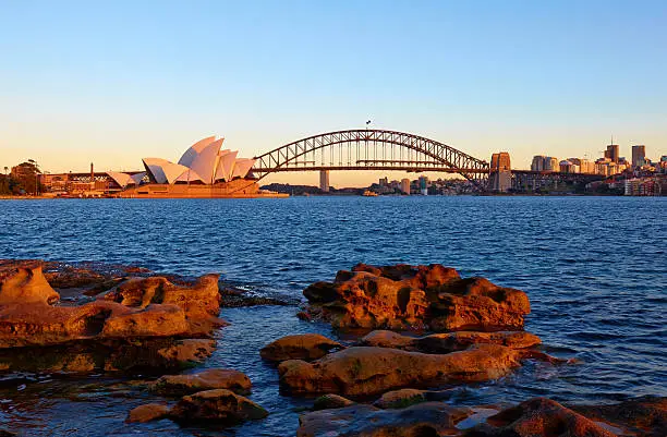 The morning sun hits Sydney's iconic Opera House and Harbour Bridge, as seen from the rocks of Mrs Macquarie's Point.
