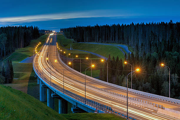 istock Overpass and light trails at night on illuminated highway forest. 612844236