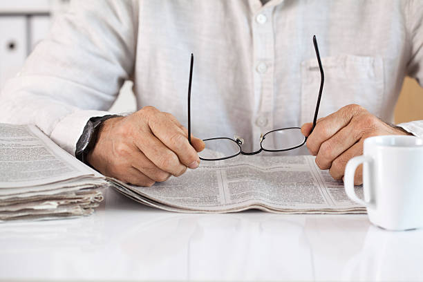 istock Man reading newspaper and holding eyeglasses 612844326