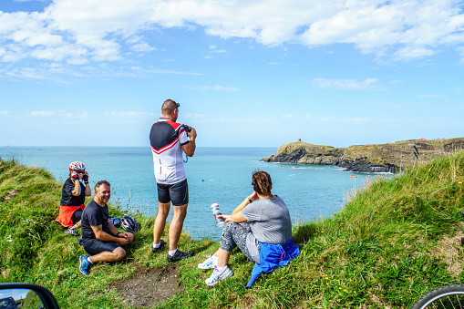 Abereiddi, UK - September 10, 2016: Four cyclists taking a break on Welsh coastline. Three are sitting and one is standing taking a photo of the bay at Abereiddi