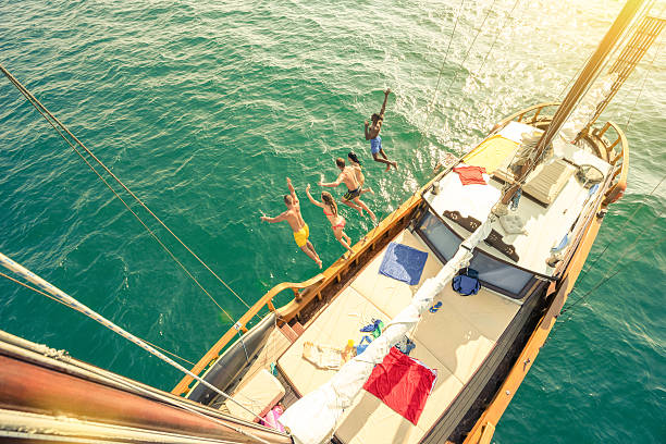 aerial view of young people jumping from sailboat sea trip - passenger ship sunset summer sun imagens e fotografias de stock