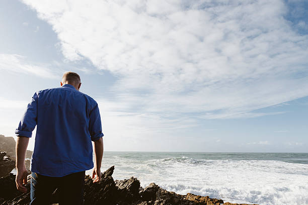 istock Man walking across rocks at the shoreline 612854432