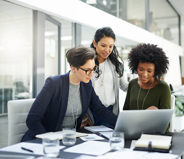 Success is a collaborative effort Shot of a group of businesswomen using a laptop during a meeting at work multiracial group stock pictures, royalty-free photos & images