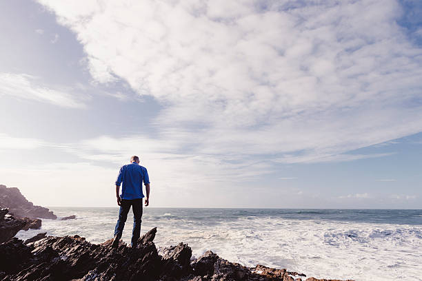 istock man standing on rocks on the shoreline looking out. 612854436