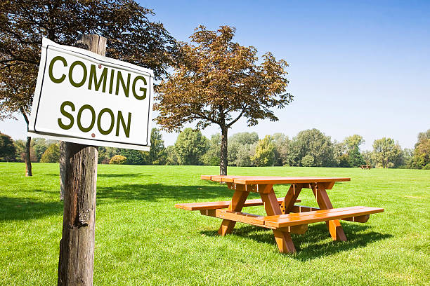 Coming soon written on a signboard near a picnic table Coming soon written on a signboard near a picnic table on a green meadow - concept image picnic photos stock pictures, royalty-free photos & images