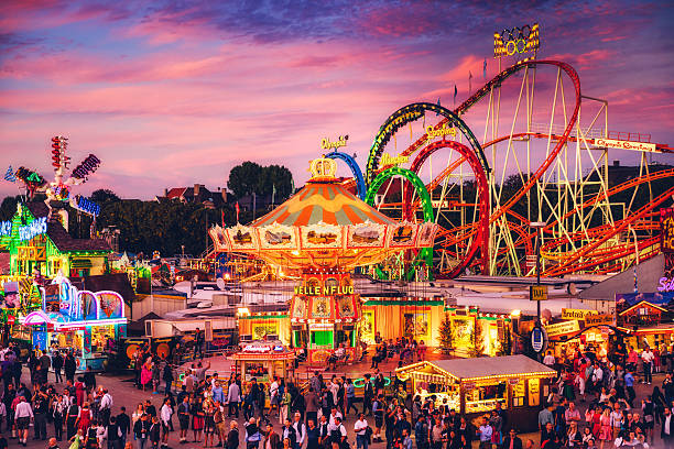 Munich, Germany - September 29, 2016: Visitors Walking Through Oktoberfest Fairgrounds, view of rotating swing ride against dusky sky.