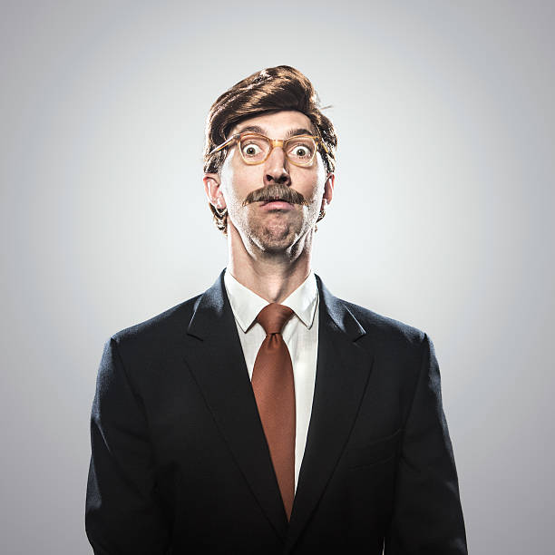 A corporate manager type business man in full suit, big combover hairstyle and mustache looks at the camera with a surprised expression, or look of fear.  Intentional cliche look for humor.  Square portrait.