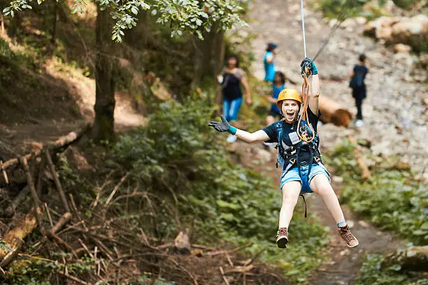 happy woman on tyrolean traverse enjoying adventure, looking at camera with arms raised and feeling free.