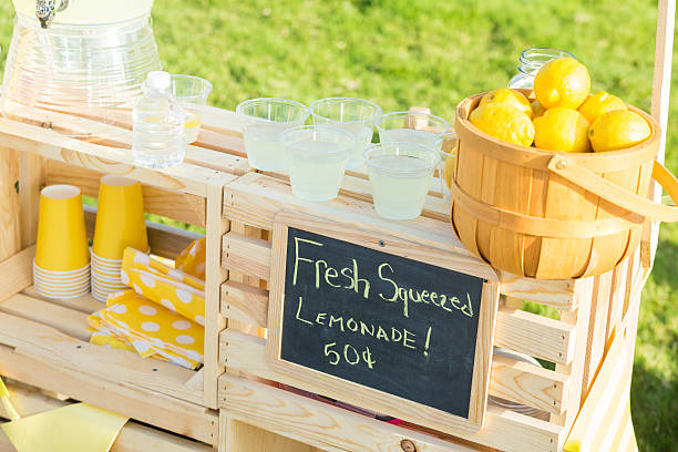 Neighborhood lemonade stand A lemonade stand is set up in the front yard of a home in the suburbs. A basket full of fresh lemons and glasses of lemonade are sitting on the stand. A chalkboard lists the price of the lemonade. images of lemonade stands stock pictures, royalty-free photos & images