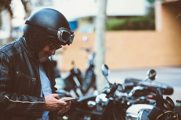 Man using a mobile phone on motorcycle Alicante, Spain - September 25, 2016: Middle aged man is using a smart phone while sitting on his motorbike on the Distinguished Gentleman's Ride day, a global fundraiser for prostate cancer and men's health investigation cafe racer stock pictures, royalty-free photos & images