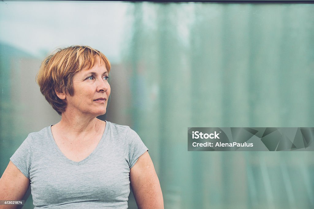 Independent Senior woman portrait - looking away, front view Independent Senior woman with short hair against window glass reflection portrait - outdoors photography. Slovenia, Europe. All logos removed. Nikon D800, full frame, Nikkor 70.0-200.0 mm, aperture 2.8, Copy space. Women Stock Photo