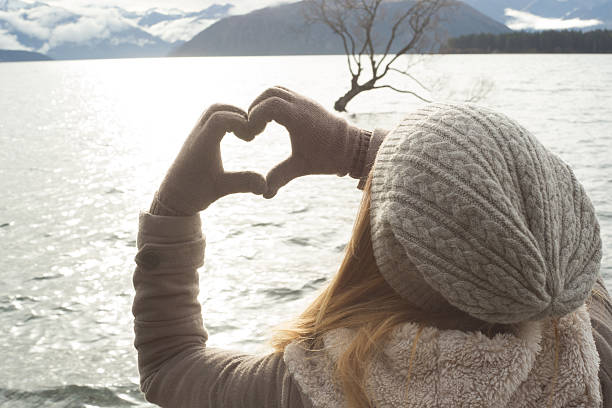 istock Young woman makes heart shape finger frame on lake Wanaka 613030740