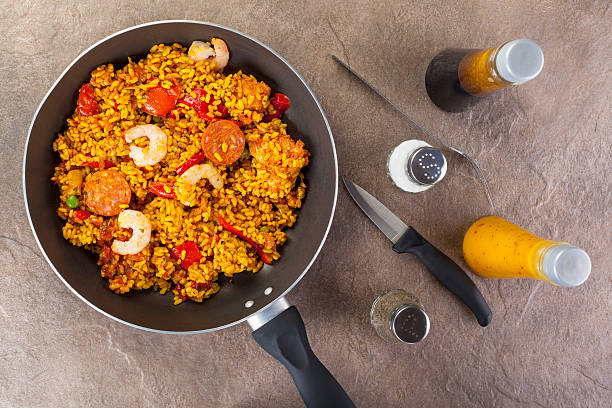 Fresh chorizo, chicken and king prawn paella in a saucepan on a stone worksurface with various condiments