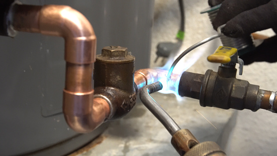 A close shot of a plumber soldering or welding together copper water piping in a residential plumbing job