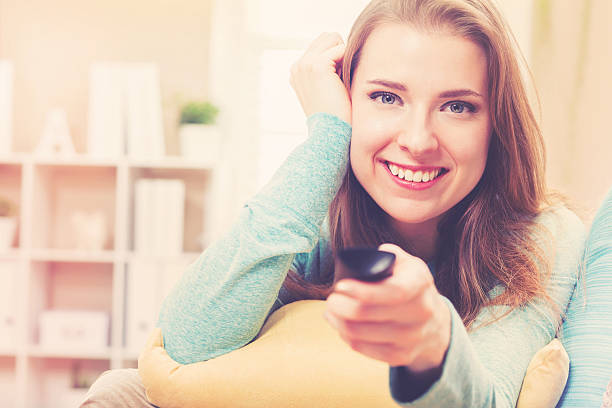 istock Young woman smiling while watching TV in her house 613042478