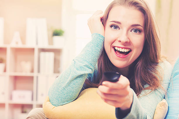 istock Young woman smiling while watching TV in her house 613042518
