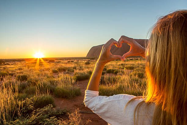 Woman frames sunset into heart shape finger frame Cheerful young woman in Australia makes a heart shape finger frame on sunset, shot in the outback. alice springs photos stock pictures, royalty-free photos & images