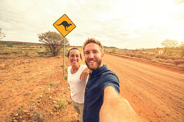 Selfie in Australia Cheerful young couple take a selfie portrait on the road standing next to a kangaroo warning sign, Australia. kangaroo crossing sign stock pictures, royalty-free photos & images