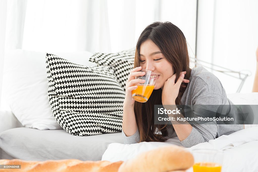 Asian girl drinking juice Asian girl laying on the bed while drinking juice Drinking Stock Photo