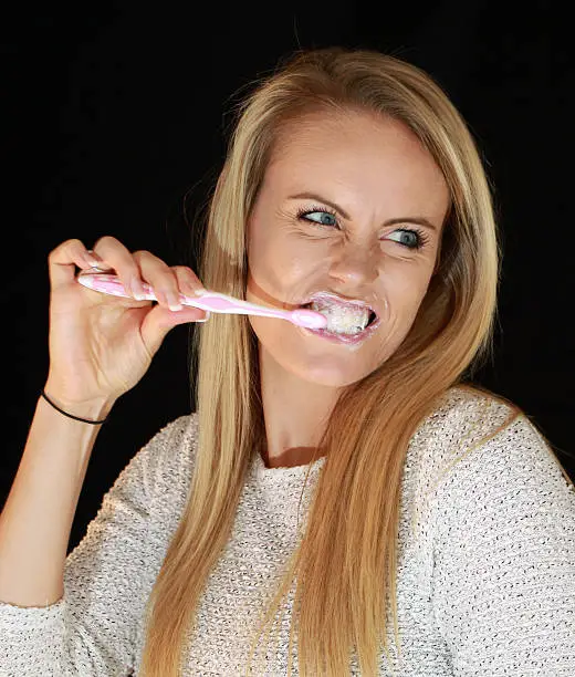 A beautiful blonde woman brushing her teeth.