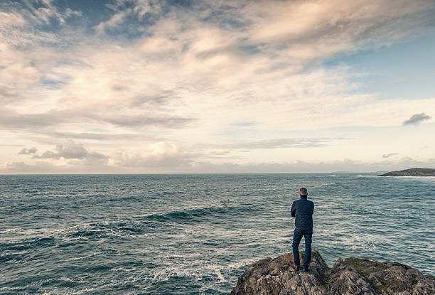 istock Man stood on rocks overlooking an open seascape. 613101782