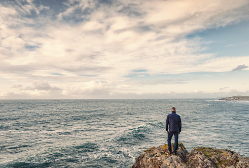 man stood looking out over an open seascape with light clouds.