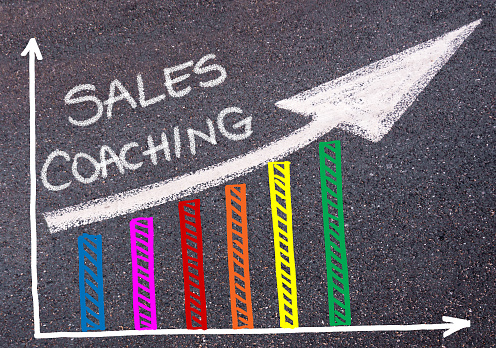 SALES COACHING written with chalk on tarmac over colorful graph and rising arrow, business marketing and creativity concept