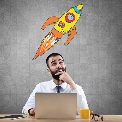 Businessman sitting at his desk with laptop and looking at rocket ship launch as new startup.