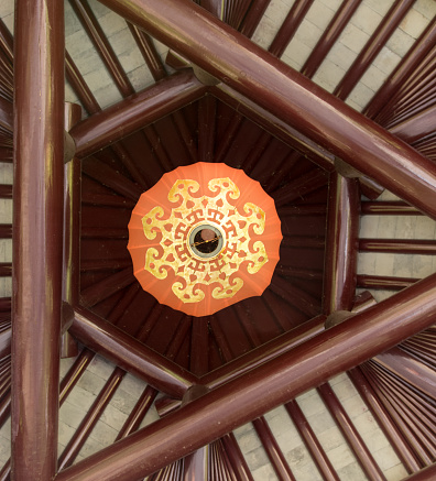 Orange chinese lampion with golden ornaments under wooden roof
