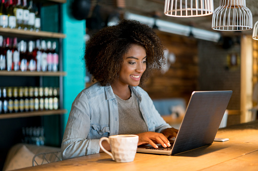 Casual woman working at a cafe using a laptop computer and looking happy