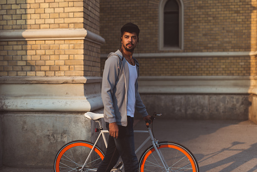 Shot of a young man walking in the city with his bike.