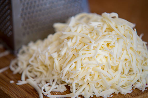 Mozzarella triturata su tagliere con grattugia - foto stock
