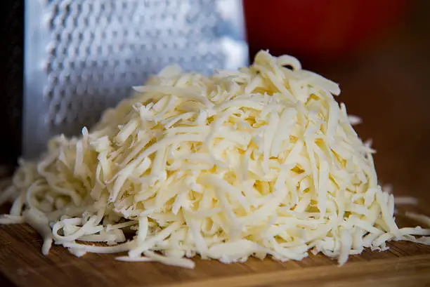 Shredded mozzarella cheese on a cutting board with a grater